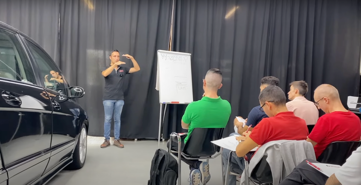 Carlo Raimondi, esperto di car detailing, spiega concetti avanzati di lucidatura e protezione auto alla lavagna durante il workshop, con studenti attenti che seguono la lezione.